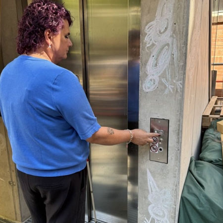 zur Seite: Bauliche Barrierefreiheit Lena stehend vor Aufzug