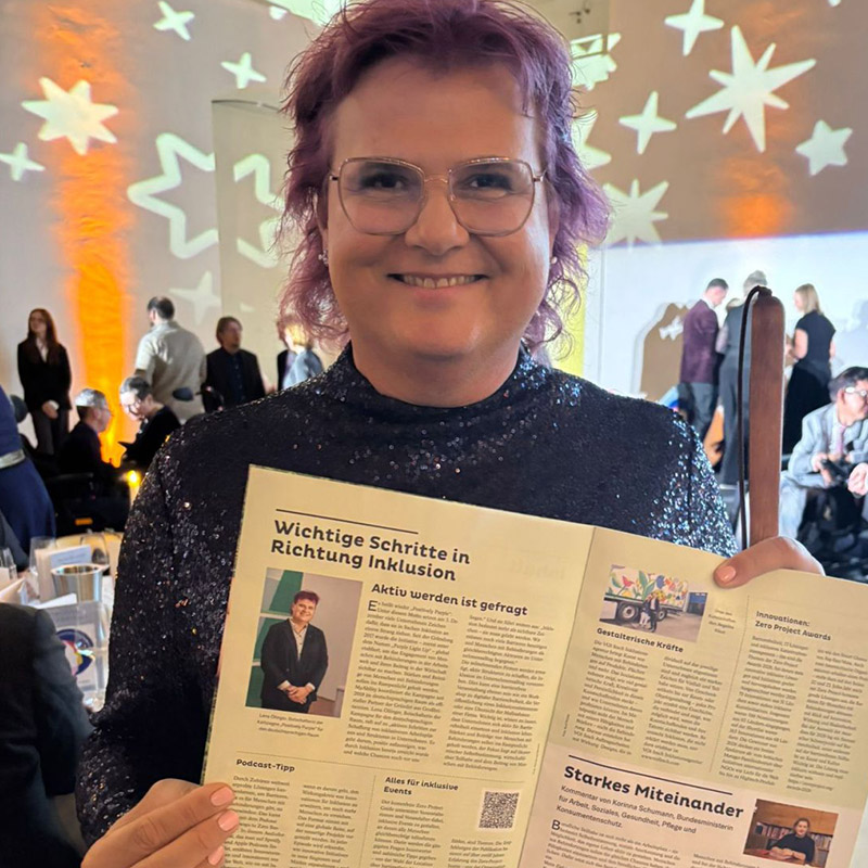 Lena auf einer Veranstaltung, hält einen Zeitungsartikel in die Kamera